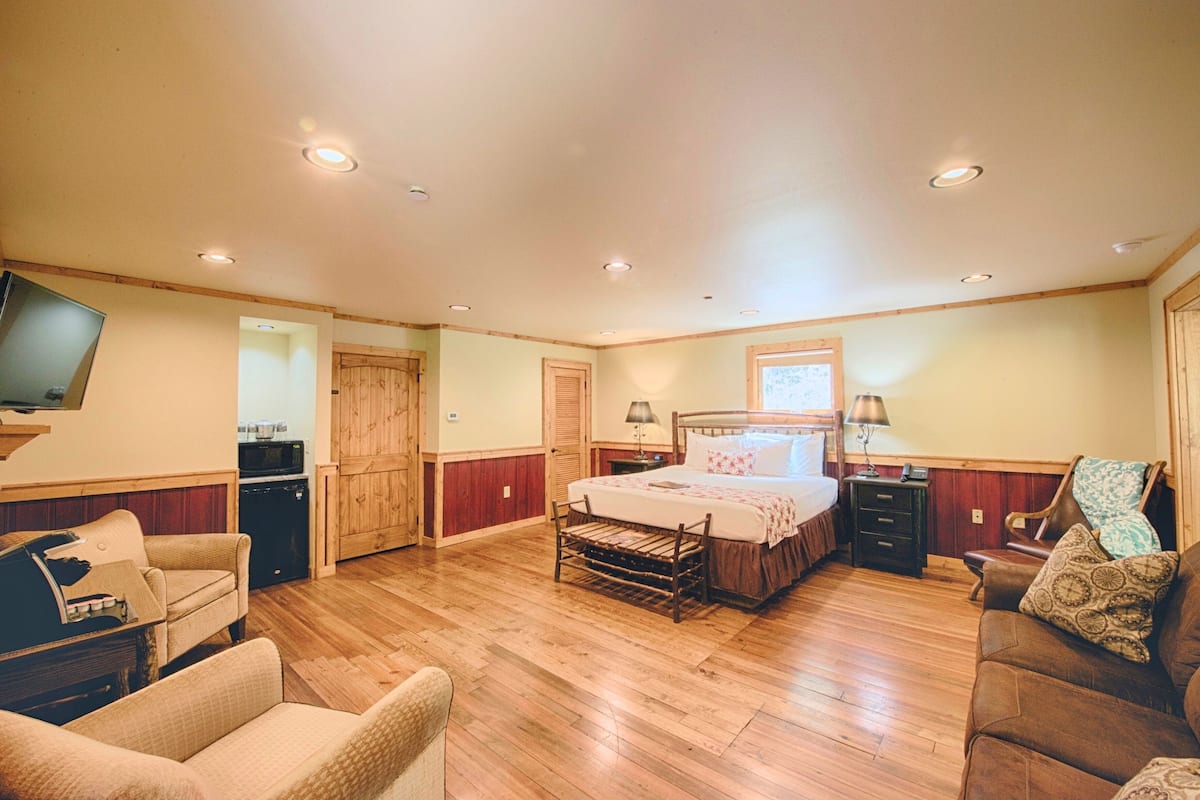 A spacious bedroom with a wooden floor, a large bed, a television, a desk, and a chair.