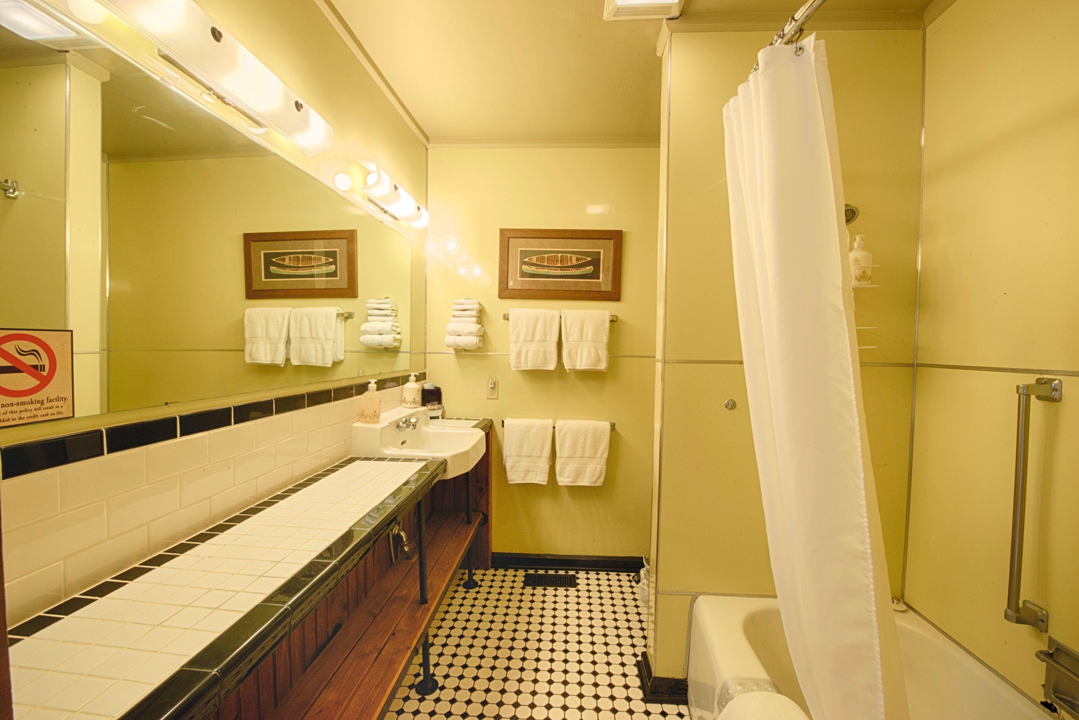 A bathroom with two sinks, a toilet, a shower, and a no-smoking sign.