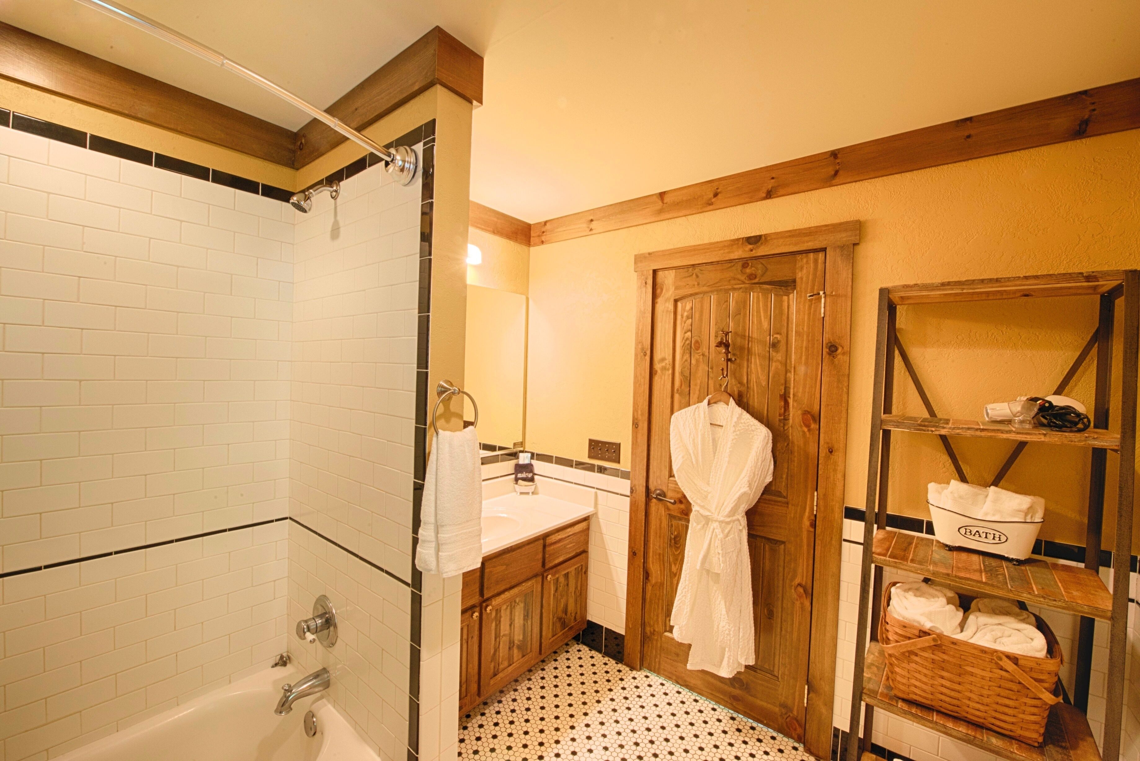A bathroom with a white bathtub, wooden vanity, and a wooden door.