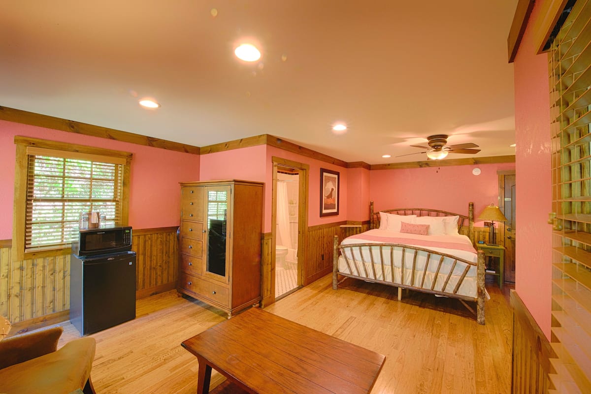 A bedroom with a bed, wooden furniture, a desk, a wardrobe, and a ceiling fan.