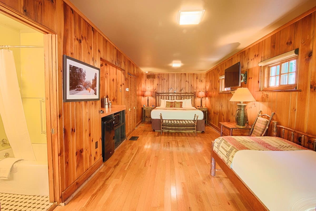 A wooden-paneled room with a bed, bedside tables, a lamp, and a television.