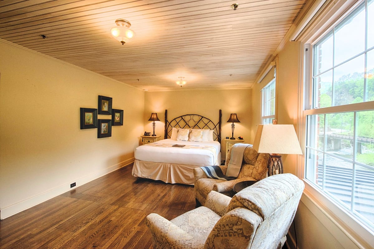 A bedroom with a large bed, two bedside tables with lamps, a chair, and a window with a view.