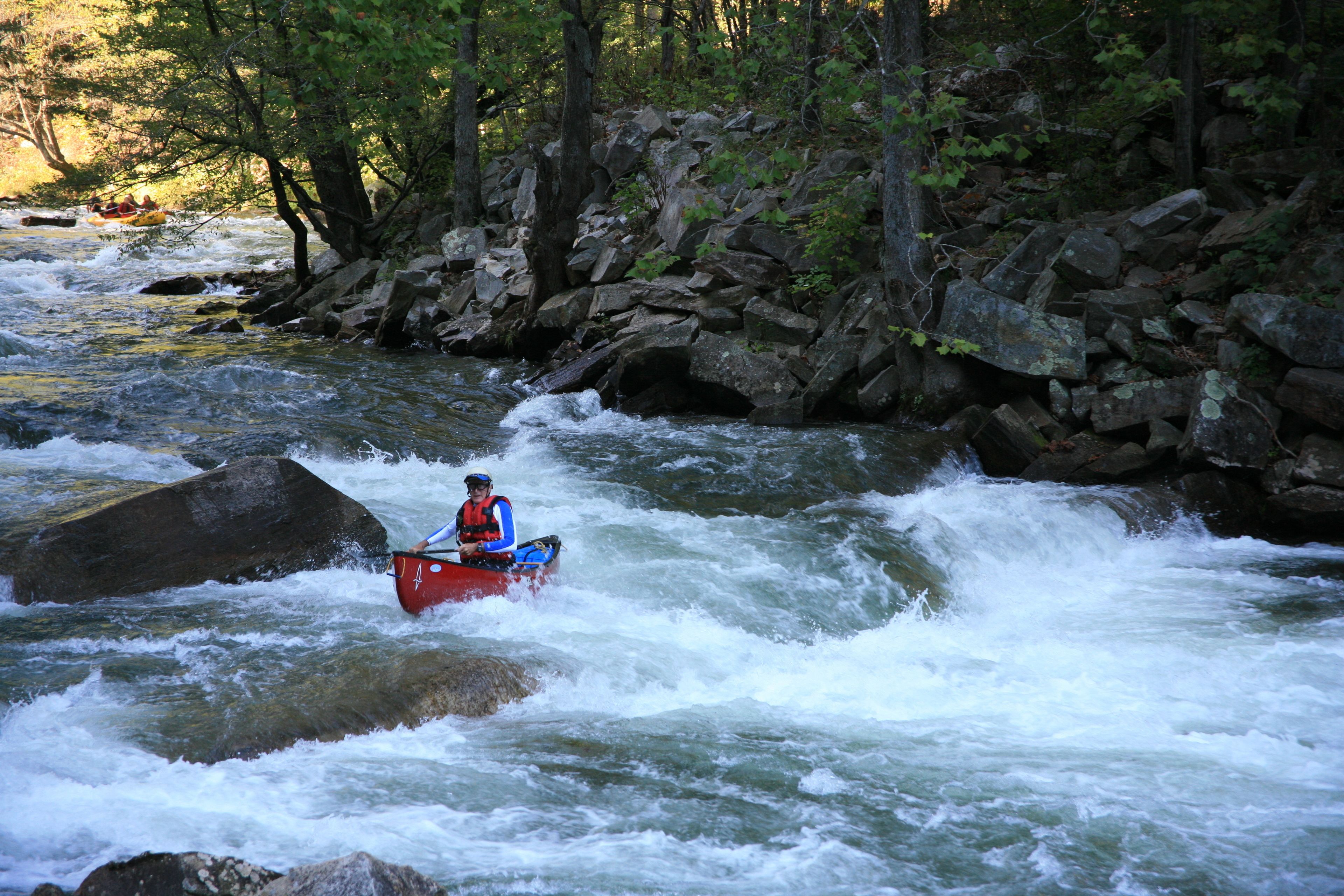 Una persona en un kayak rojo navegando por un río rodeado de rocas y árboles.