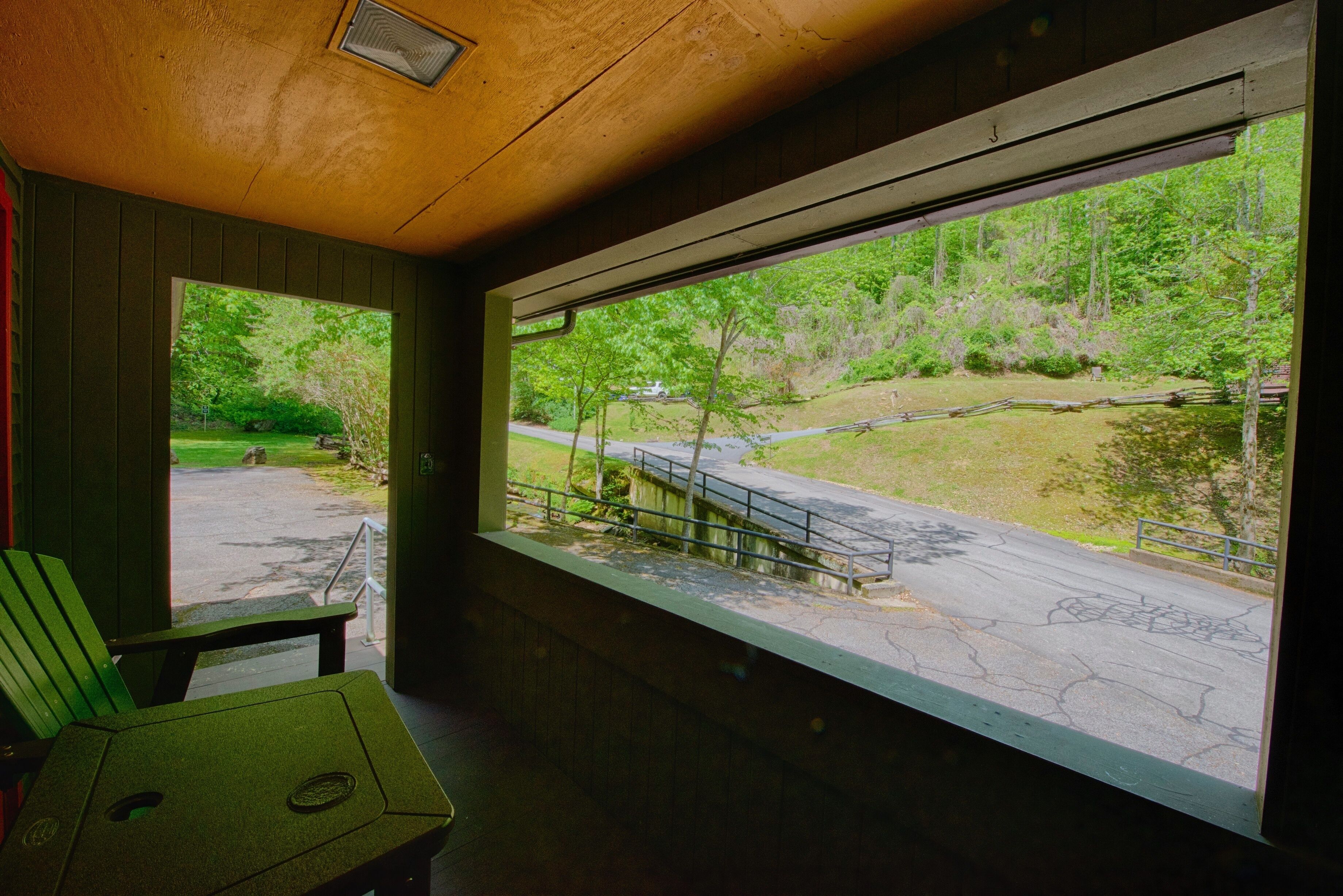 A room with a large window offering a view of a park with a pathway and trees.