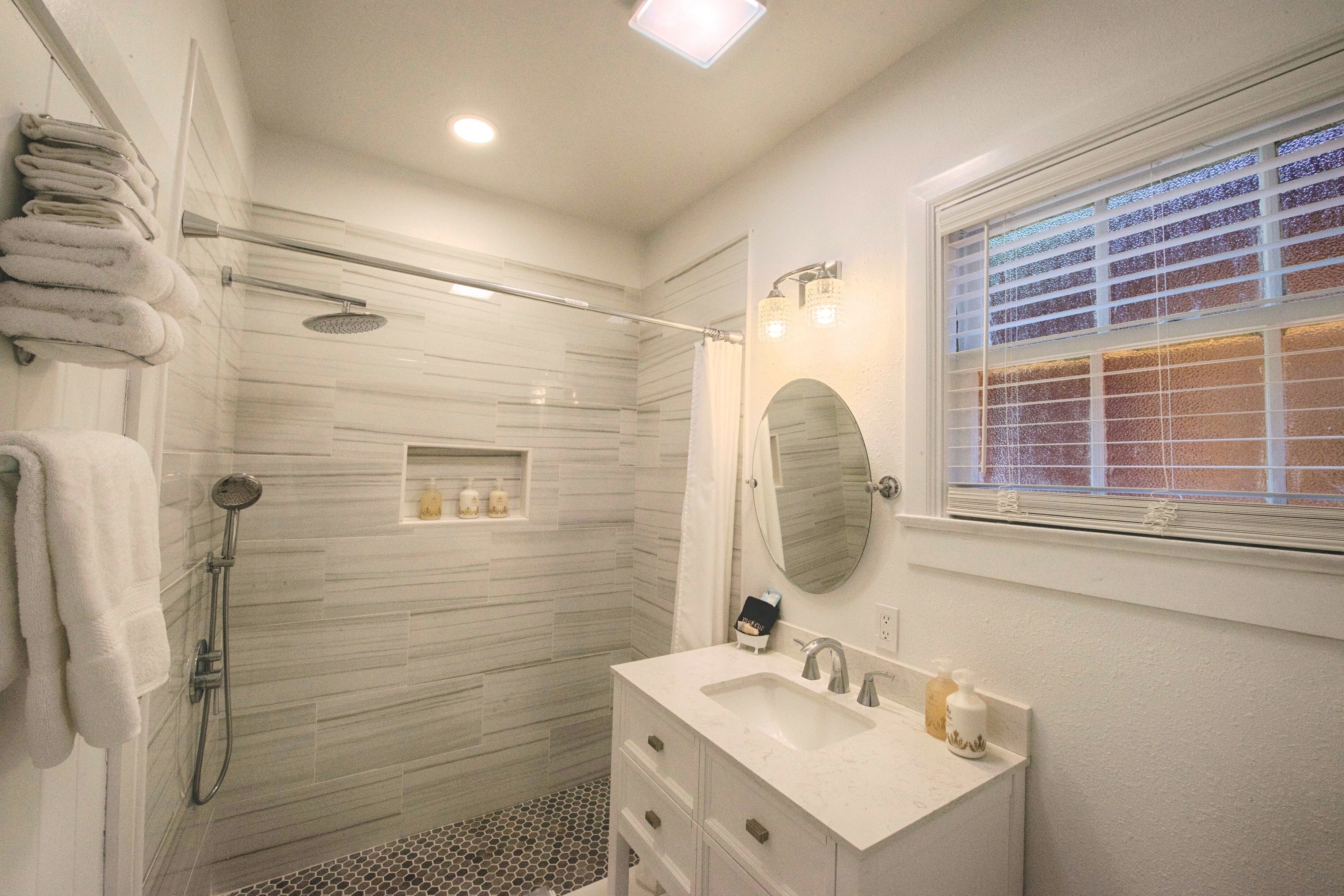 Un baño moderno con ducha envuelta en vidrio, tocador con espejo y ventana con persianas.