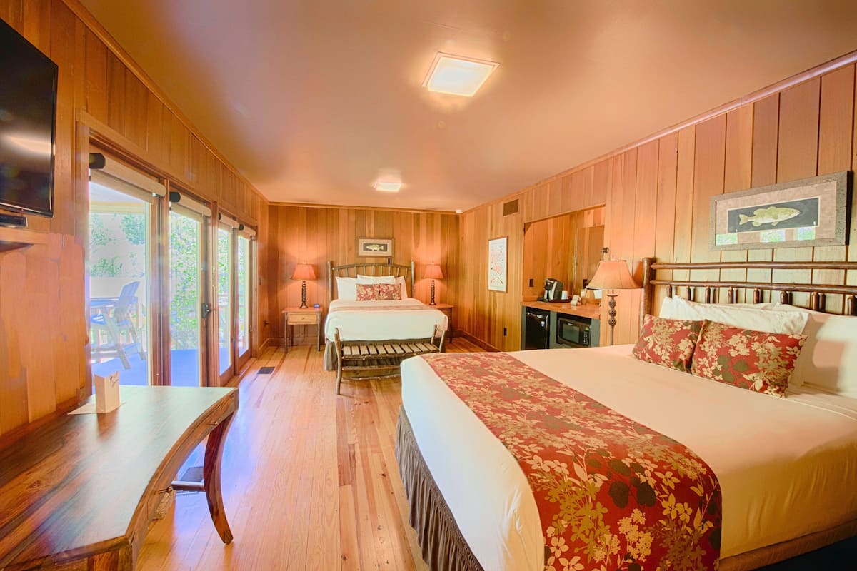 A wooden-paneled room with two beds, a desk, and a TV.