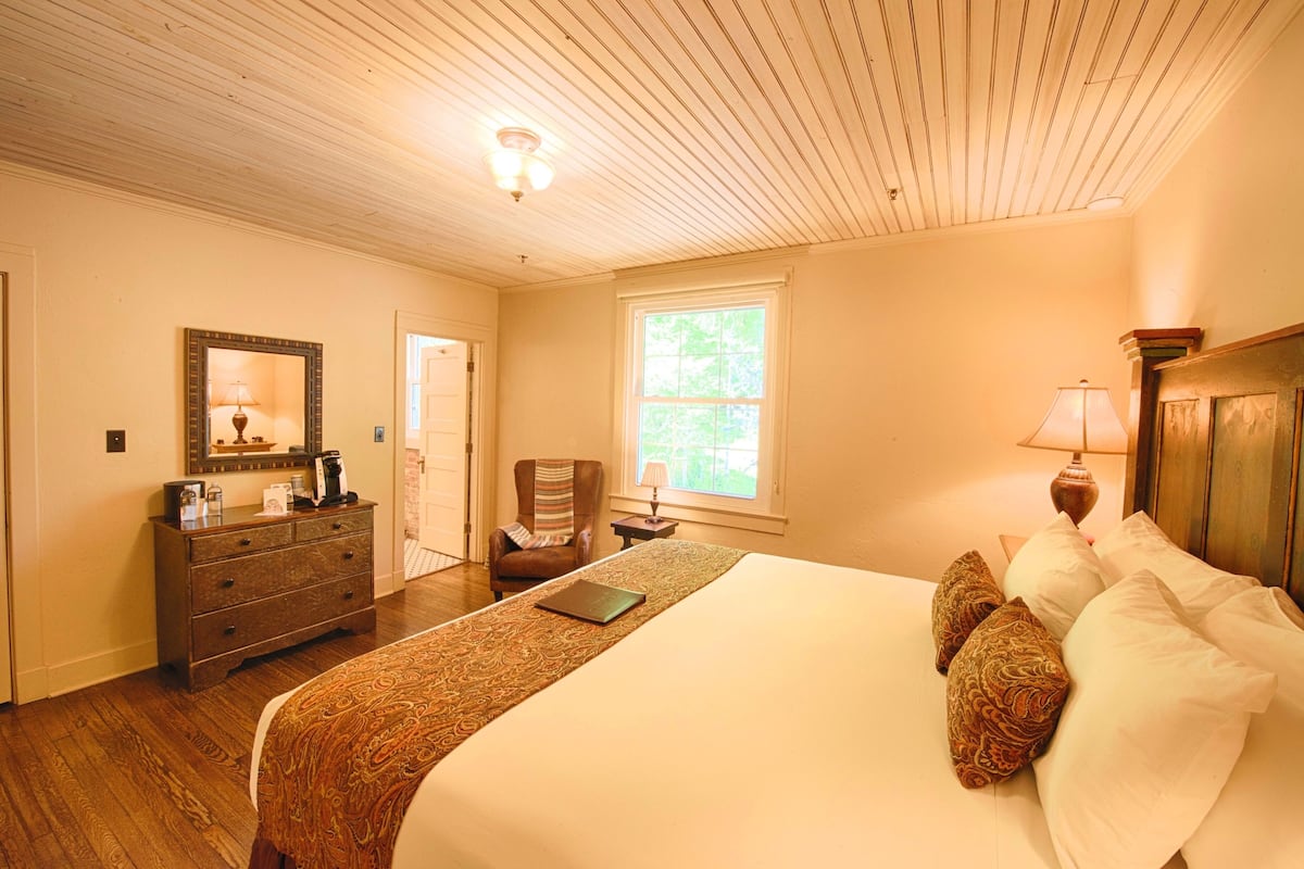 A bedroom with a large bed, a dresser, a chair, and a window.