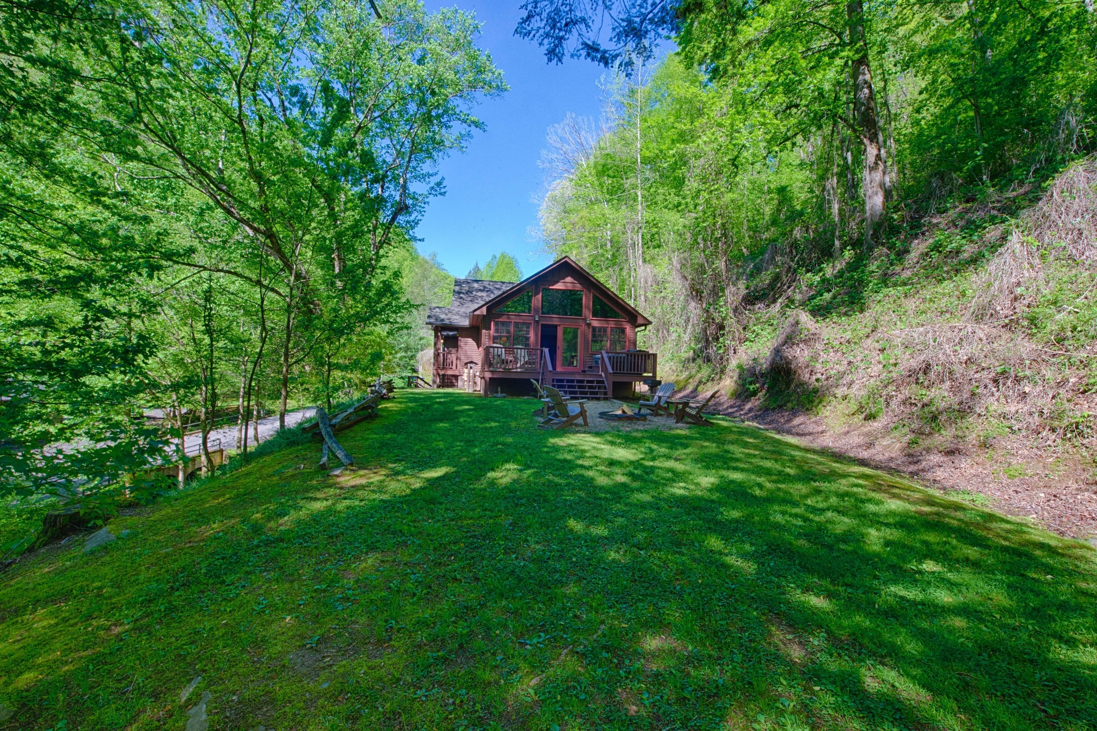 A cabin with a deck and outdoor seating, surrounded by lush greenery and trees.
