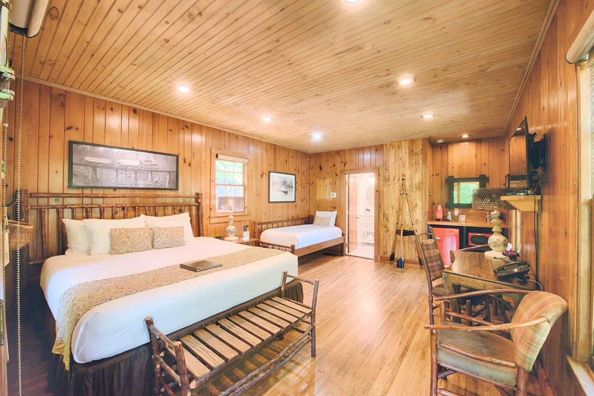 A wooden cabin-style room with two beds, a desk, and a chair.