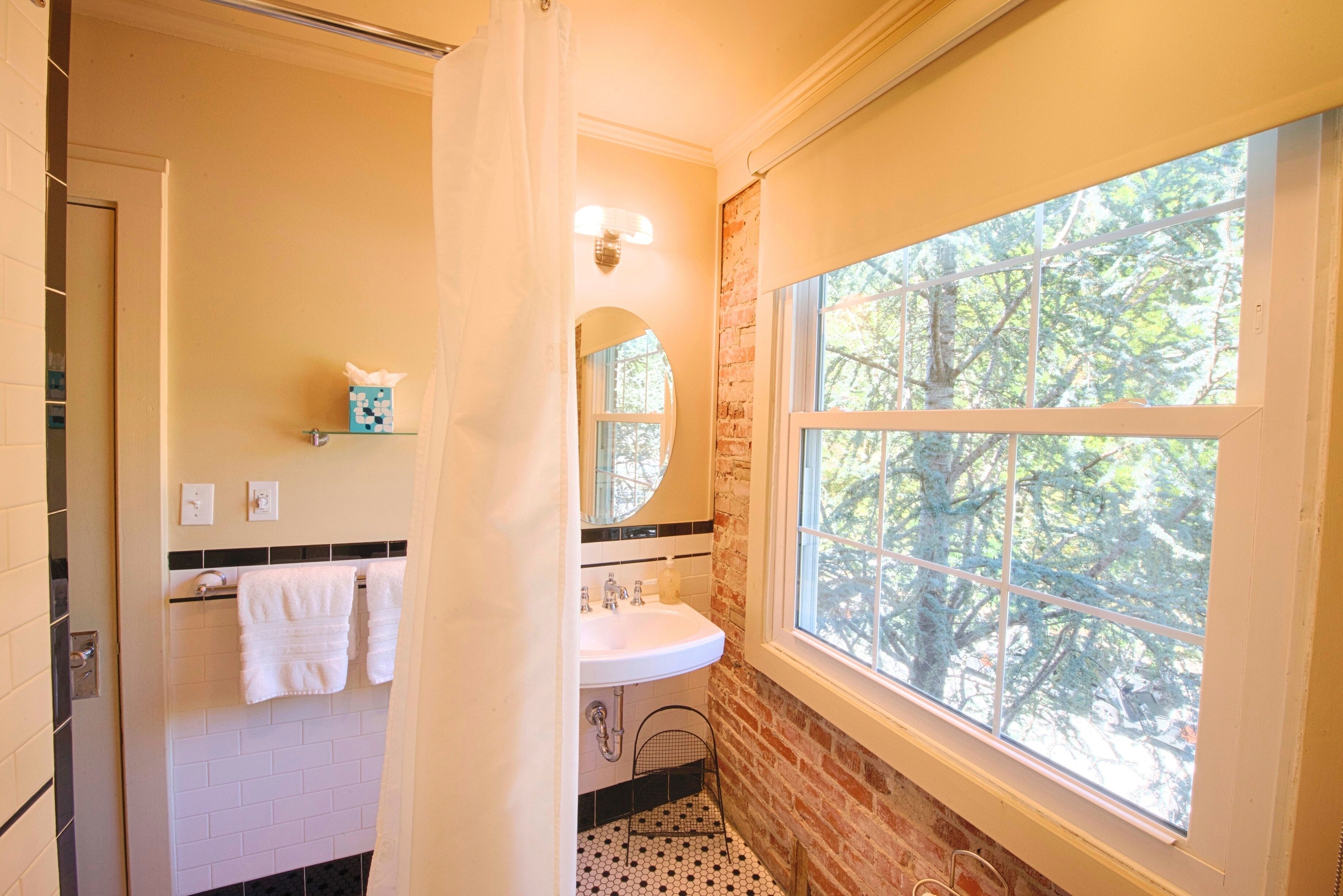 A bathroom with a white sink, a mirror, and a window with a view of trees.