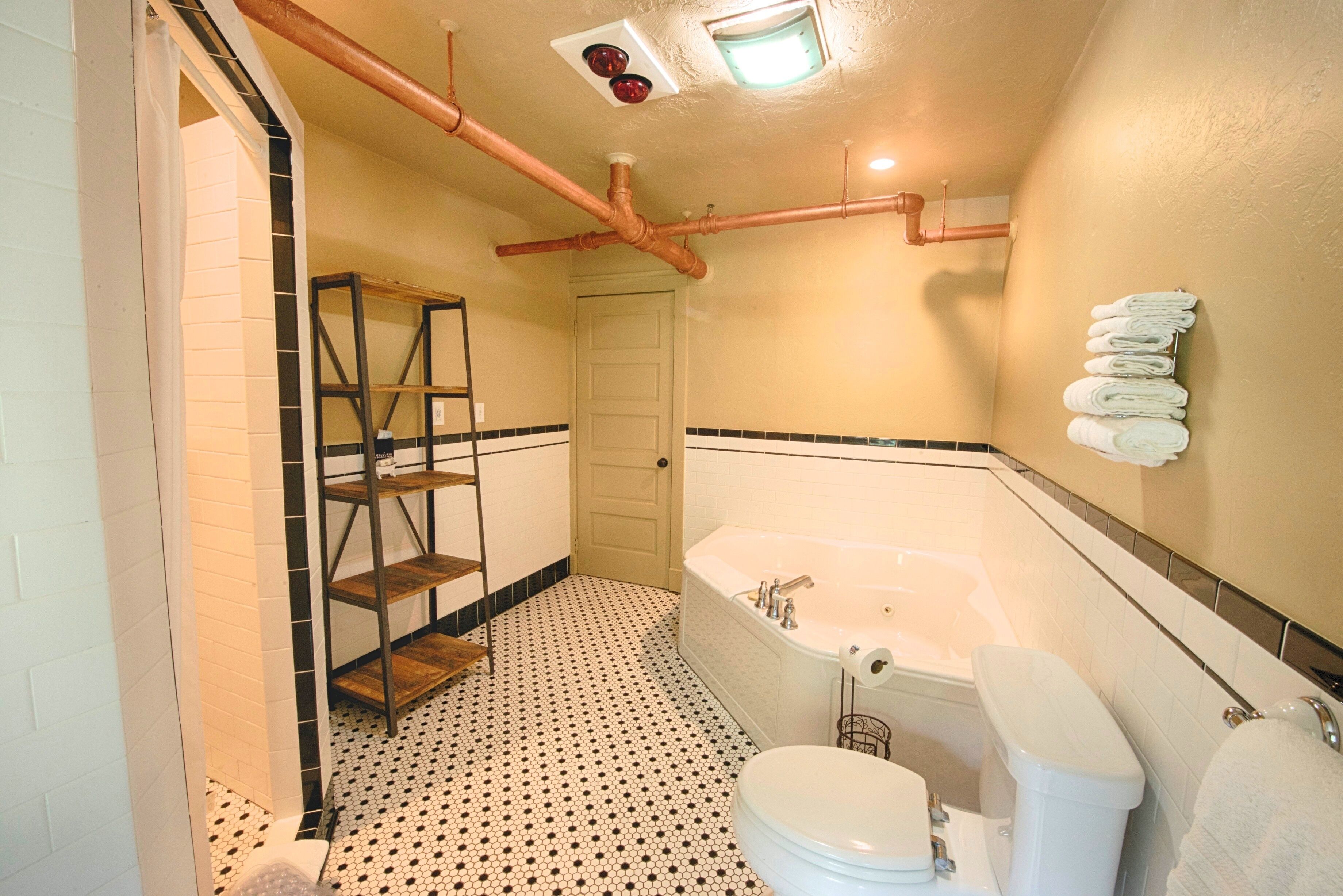 Ein Badezimmer mit Badewanne, Toilette und Duschbereich. Es gibt ein Holzbodenregal und ein Fliesenboden.