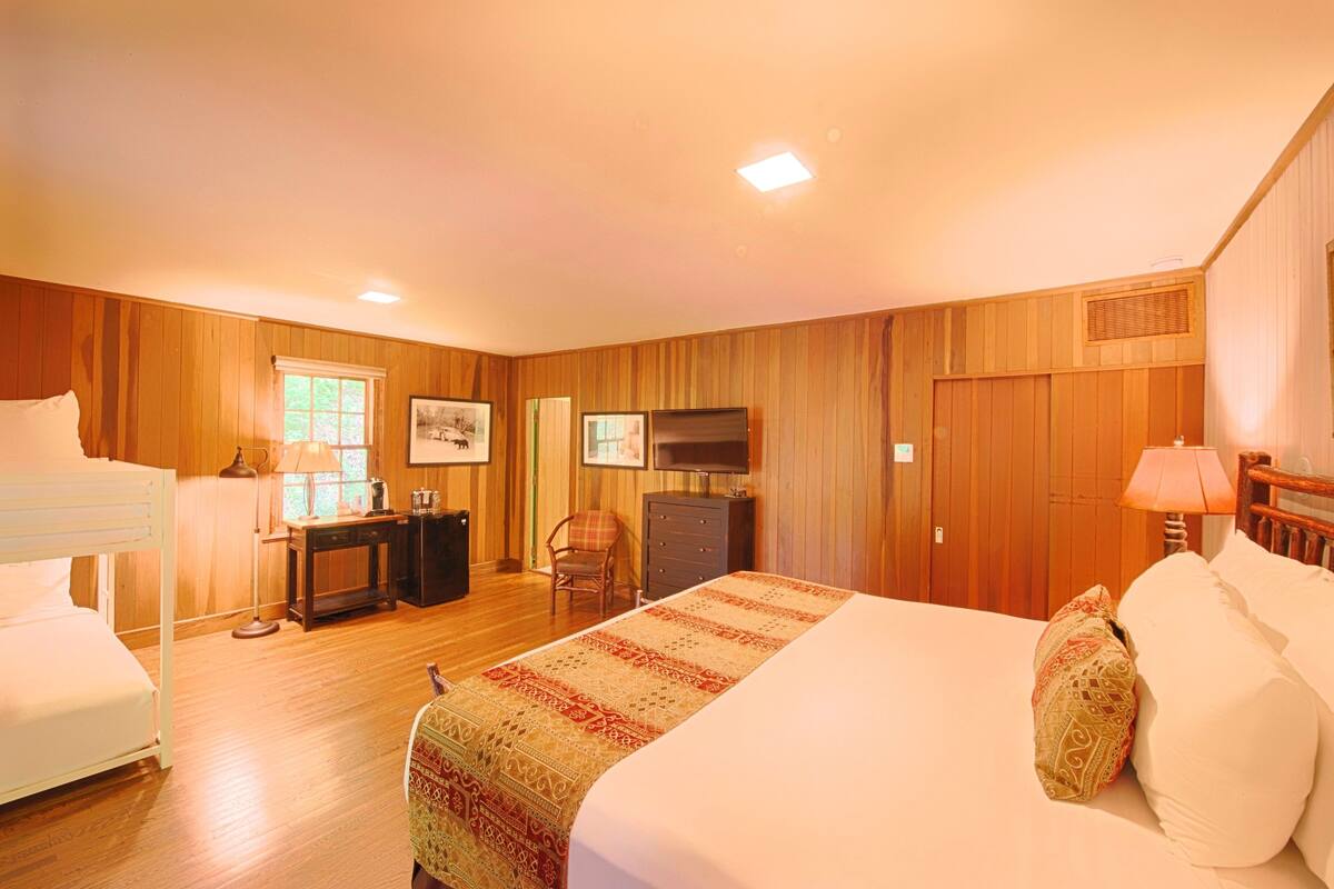 A wooden-paneled room with a bed, a desk, a chair, a television, and a wardrobe.
