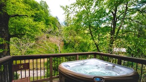 A hot tub on a wooden deck with a railing, surrounded by lush greenery. - Historic Tapoco Lodge Resort (Robbinsville)