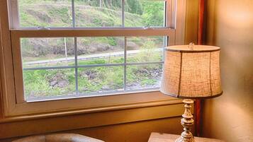 A room with a window, a chair, and a small wooden nightstand with a lamp.