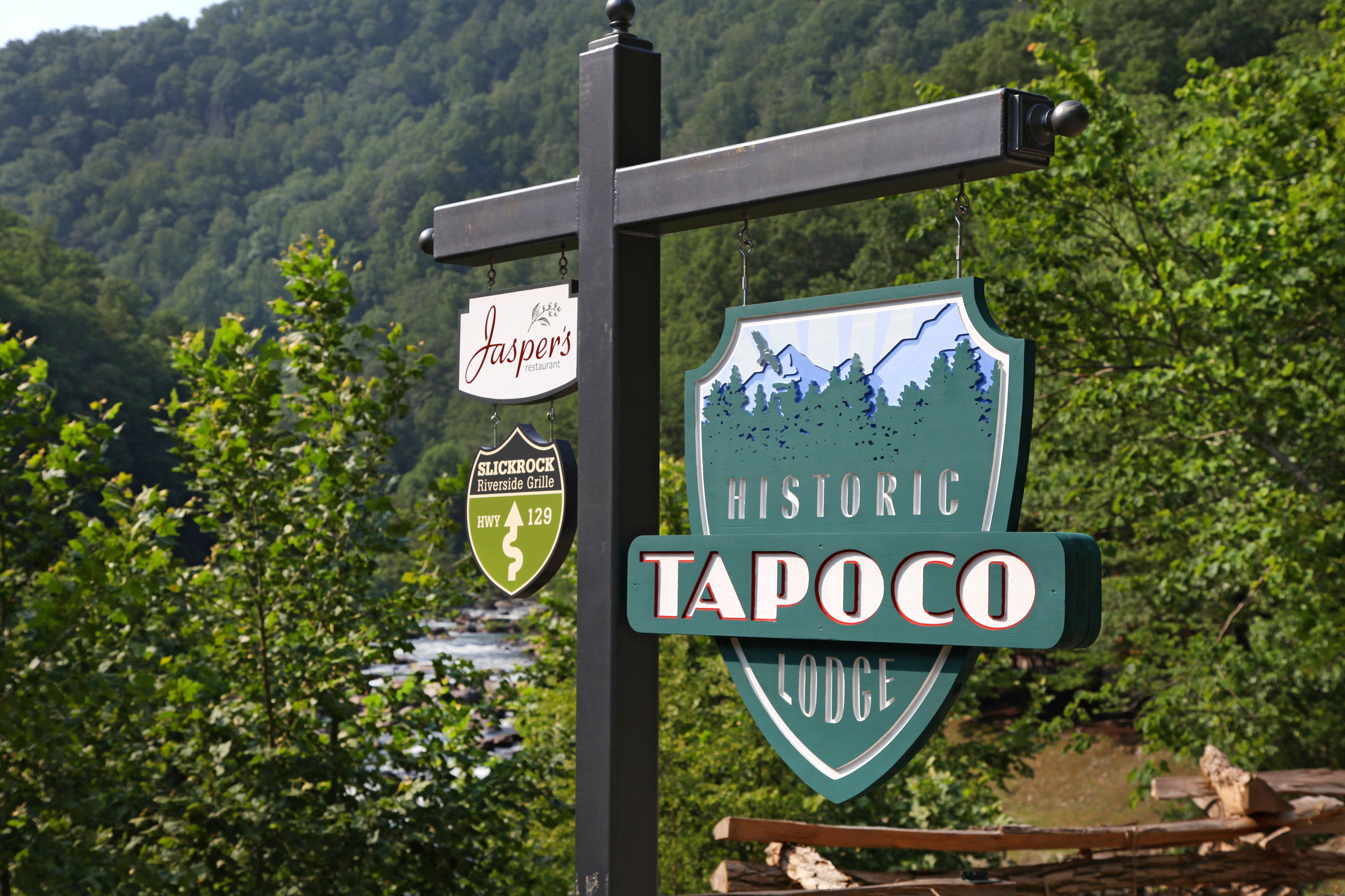 Señal del Historic Tapoco Lodge con vista a un río y un bosque al fondo.