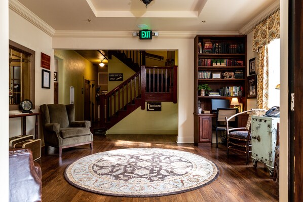 A lobby with a wooden floor, a round patterned rug, a bookshelf, a desk with a lamp, and a staircase leading to upper floors. - Historic Tapoco Lodge Resort (Robbinsville)