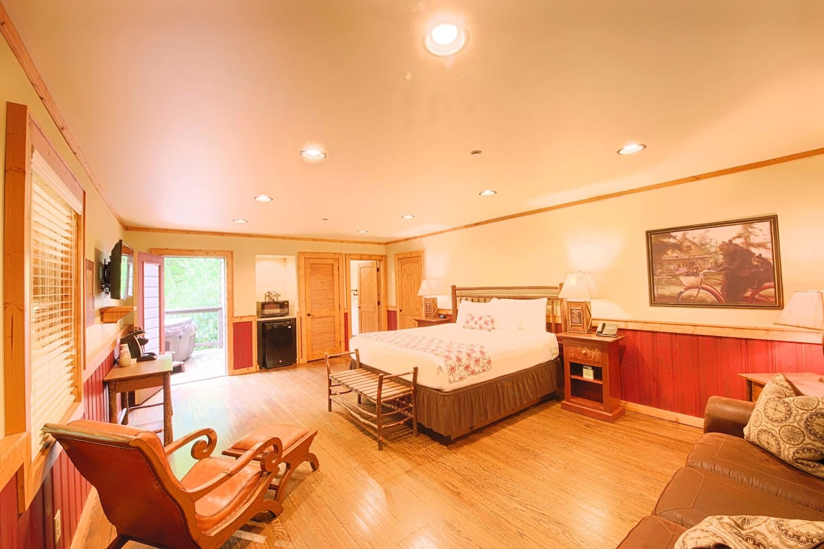 A spacious bedroom with a large bed, wooden flooring, a rocking chair, a sofa, and a painting on the wall.