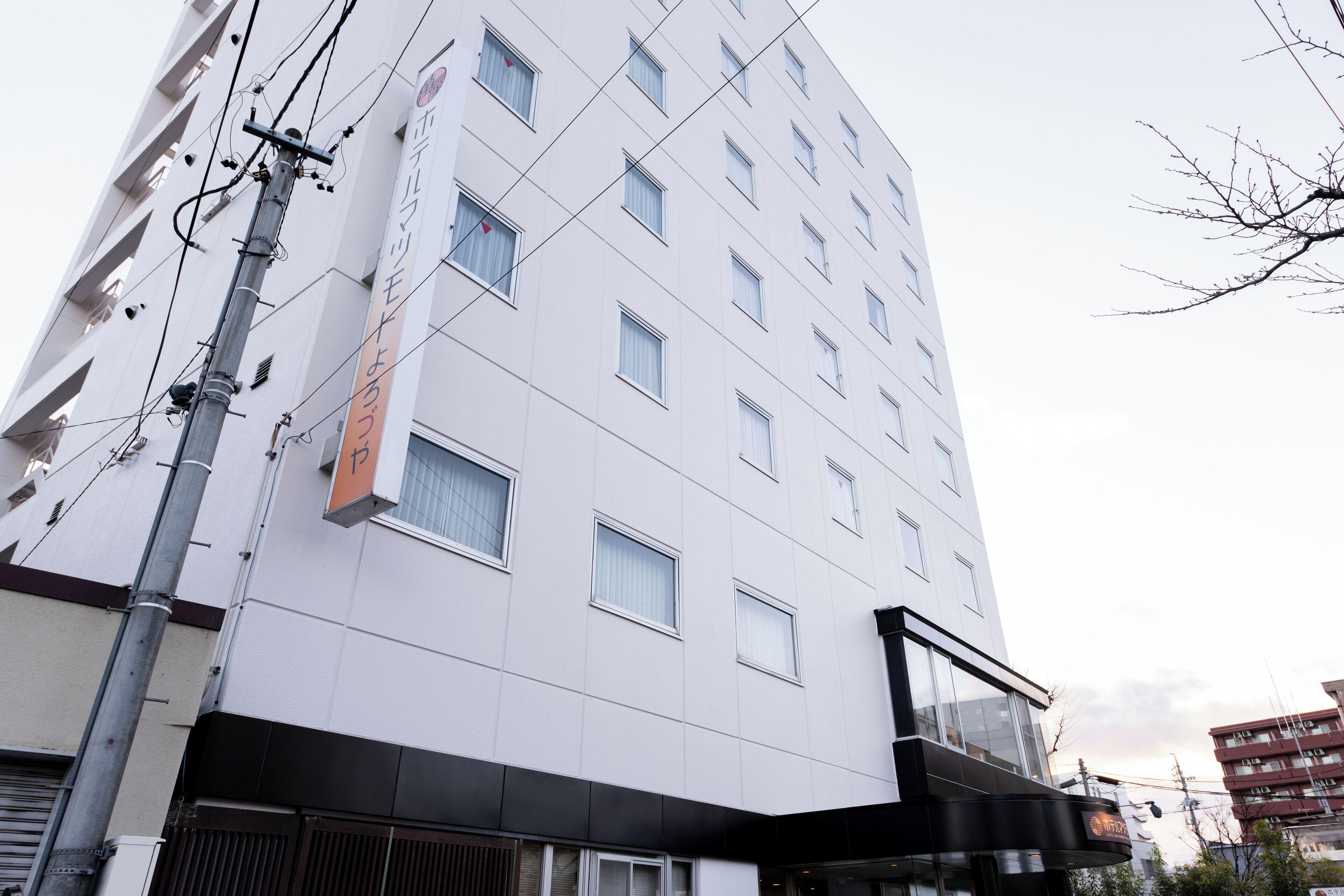 Un immeuble à plusieurs étages, doté d’une façade blanche, de nombreuses fenêtres et d’une enseigne bien visible avec des caractères japonais.