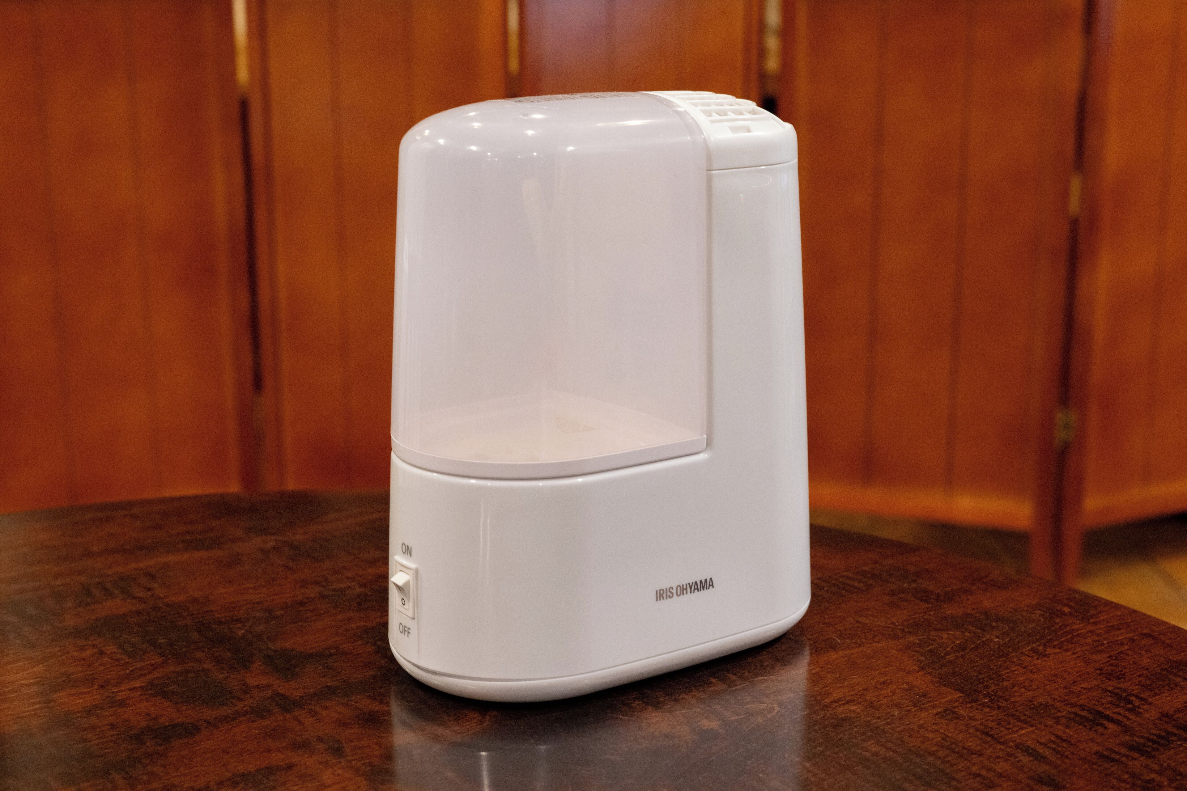 A white coffee maker on a wooden table with a wooden background.