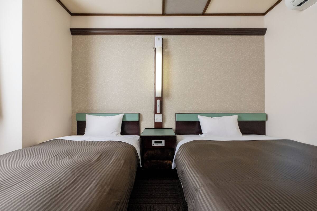 A hotel room with two single beds, a nightstand between them, and a wall-mounted light fixture.