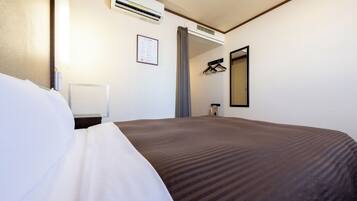 Ein Hotelzimmer mit einem großen Bett, einem Nachttisch, einer Klimaanlage, einem Spiegel und einem an der Wand befestigten Kleiderhaken.