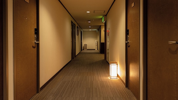 Un couloir d’hôtel avec des portes des deux côtés, un sol recouvert de moquette et un luminaire sur le côté droit.