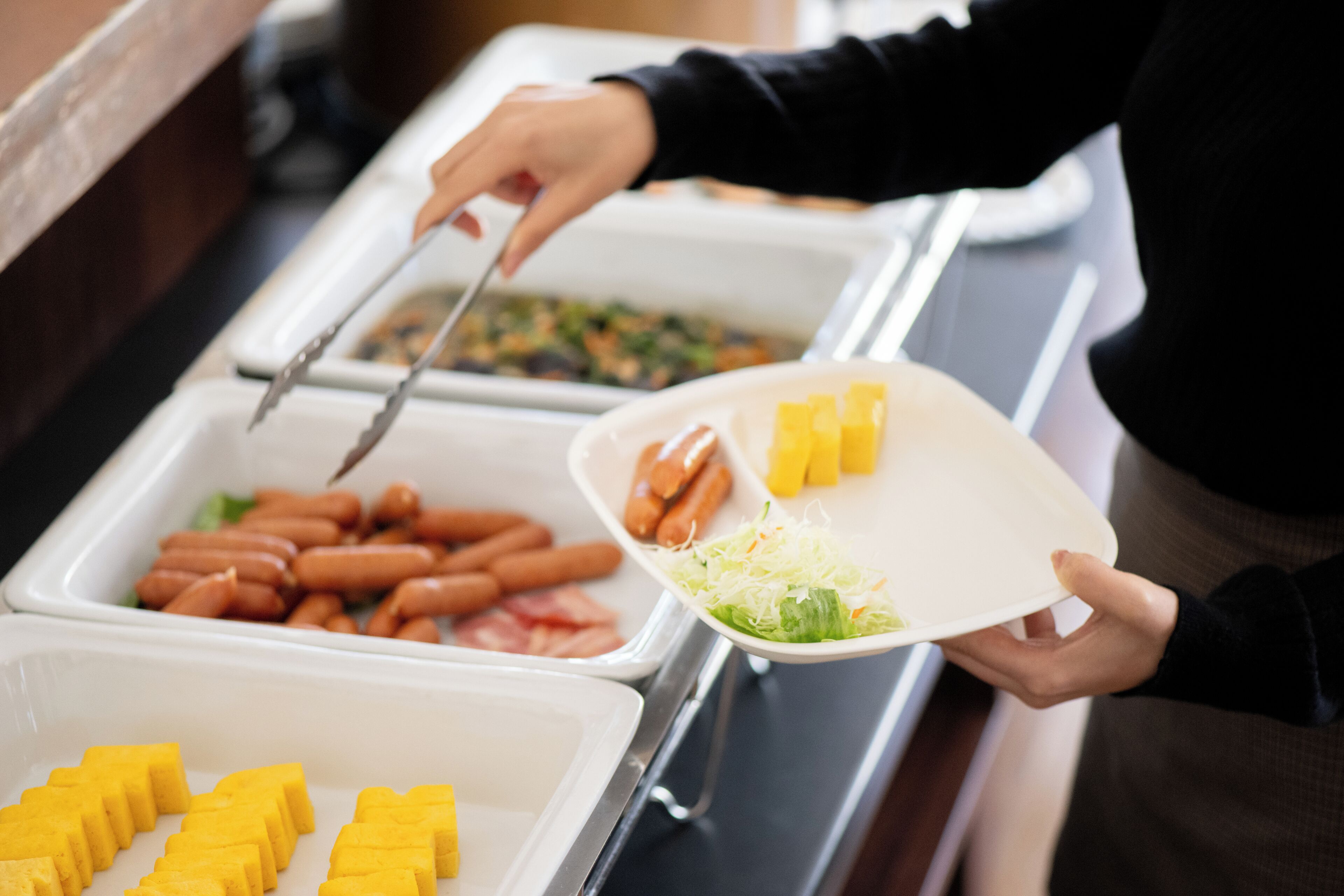 A buffet setup with various food items including hot dogs, cheese, and salad.