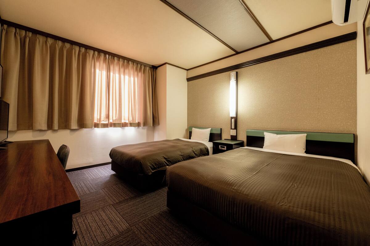 A hotel room with two beds, a desk, and a large window with curtains.