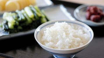 Un bol de riz blanc sur une table, avec une assiette de sushis et une assiette de légumes marinés en arrière-plan.