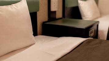 A hotel room with a bed, green headboard, white pillow, and a nightstand with a small drawer.