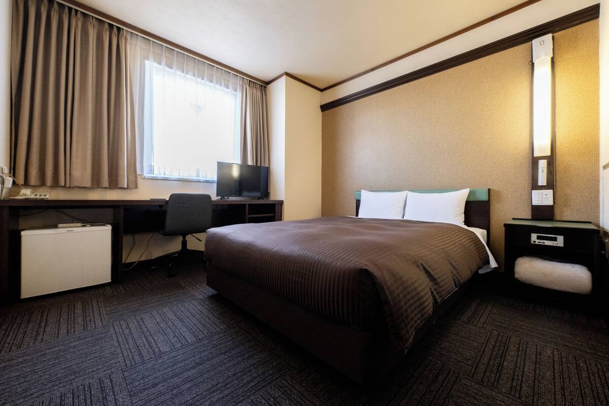 A hotel room with a bed, a desk, a television, and a small refrigerator.