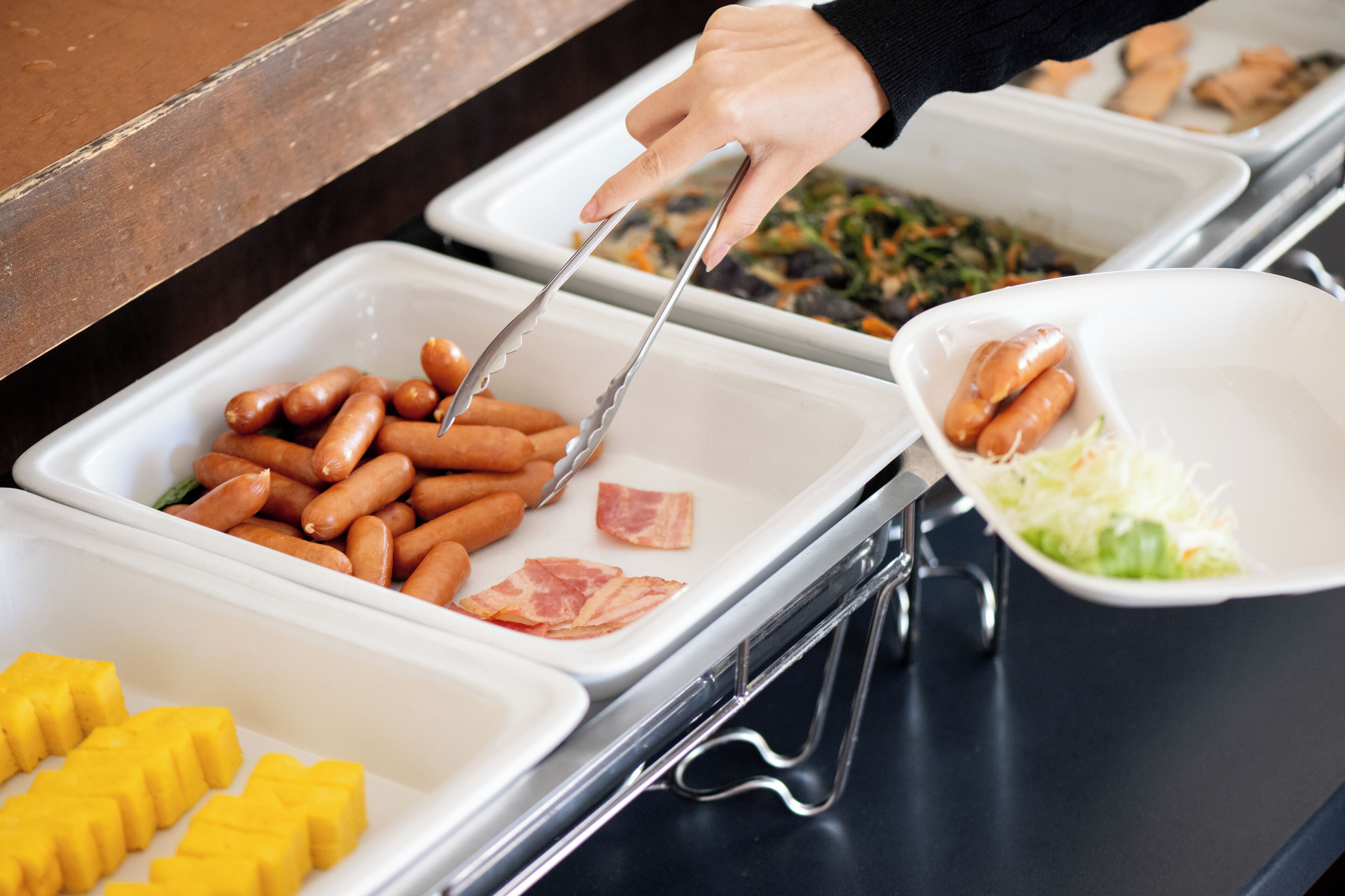 A buffet with various food items including sausages, bacon, and coleslaw.