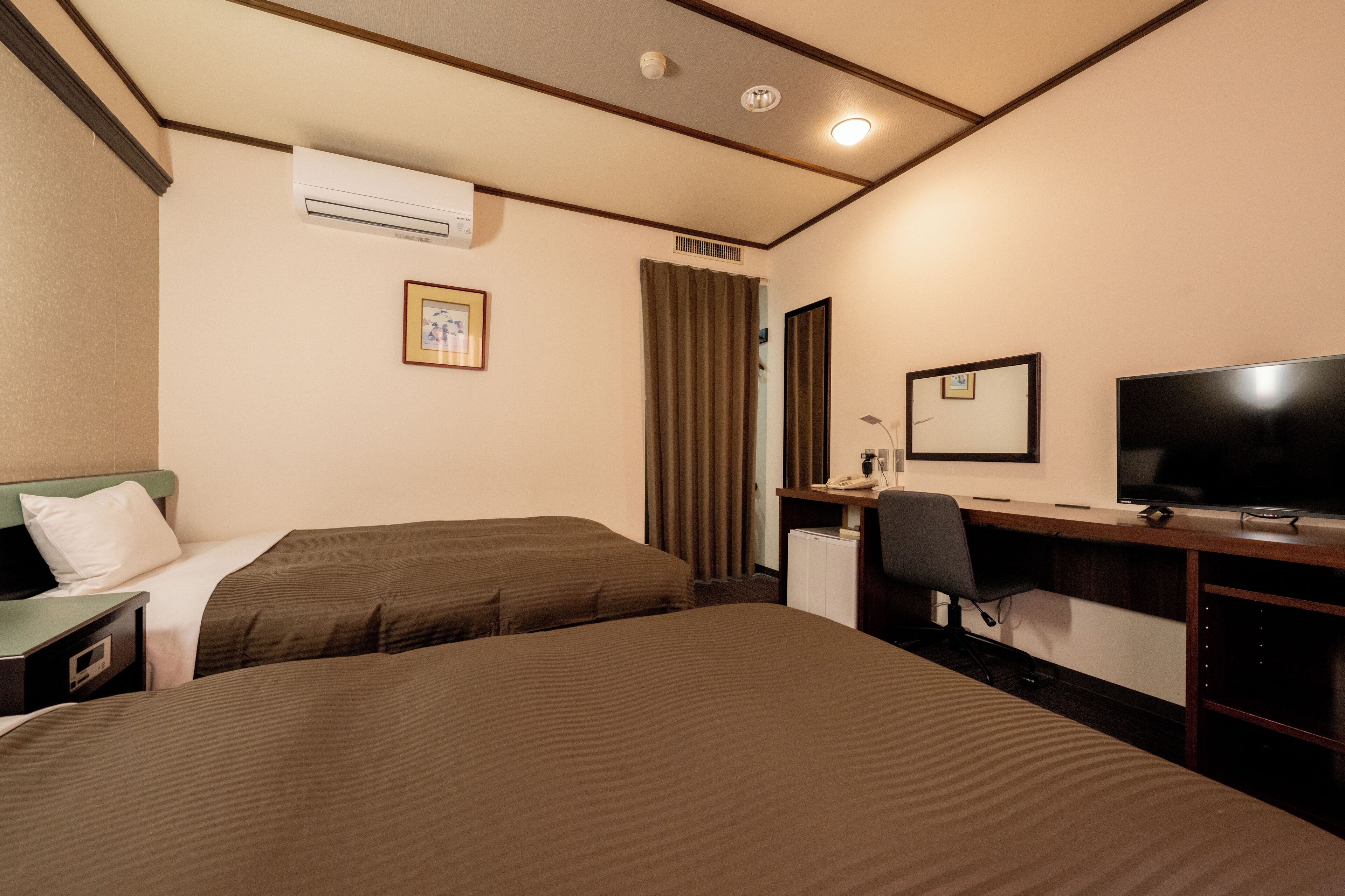 A hotel room with two beds, a desk with a chair, a television, and an air conditioning unit.