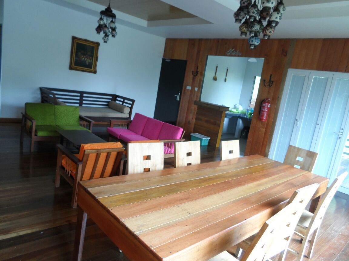 Ein Essbereich mit Holztisch und -stühlen, einer Couch mit Kissen sowie einer hängenden Leuchte.