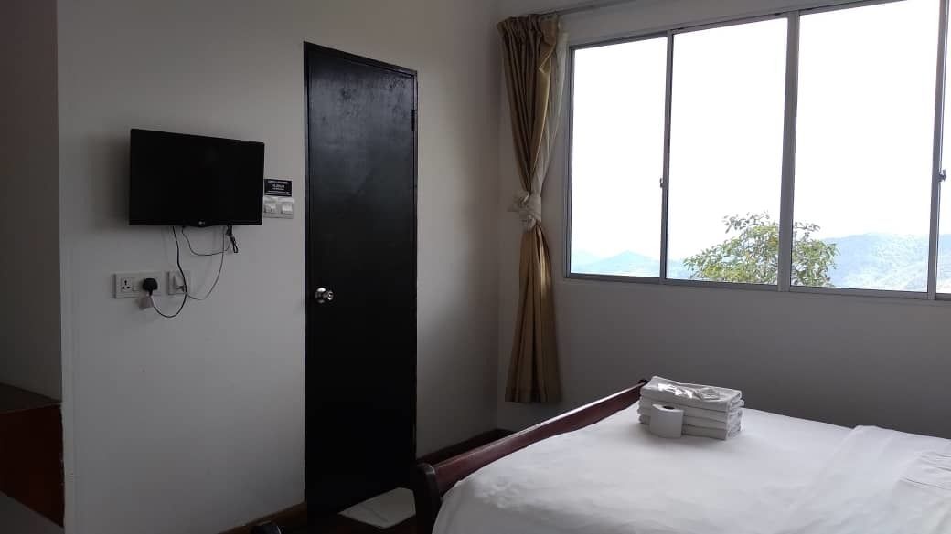 A hotel room with a bed, a TV mounted on the wall, a window with curtains, and a view of the outdoors.