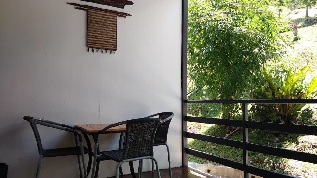 Un balcon avec deux chaises et une petite table, donnant sur un jardin où poussent différentes plantes et arbres.