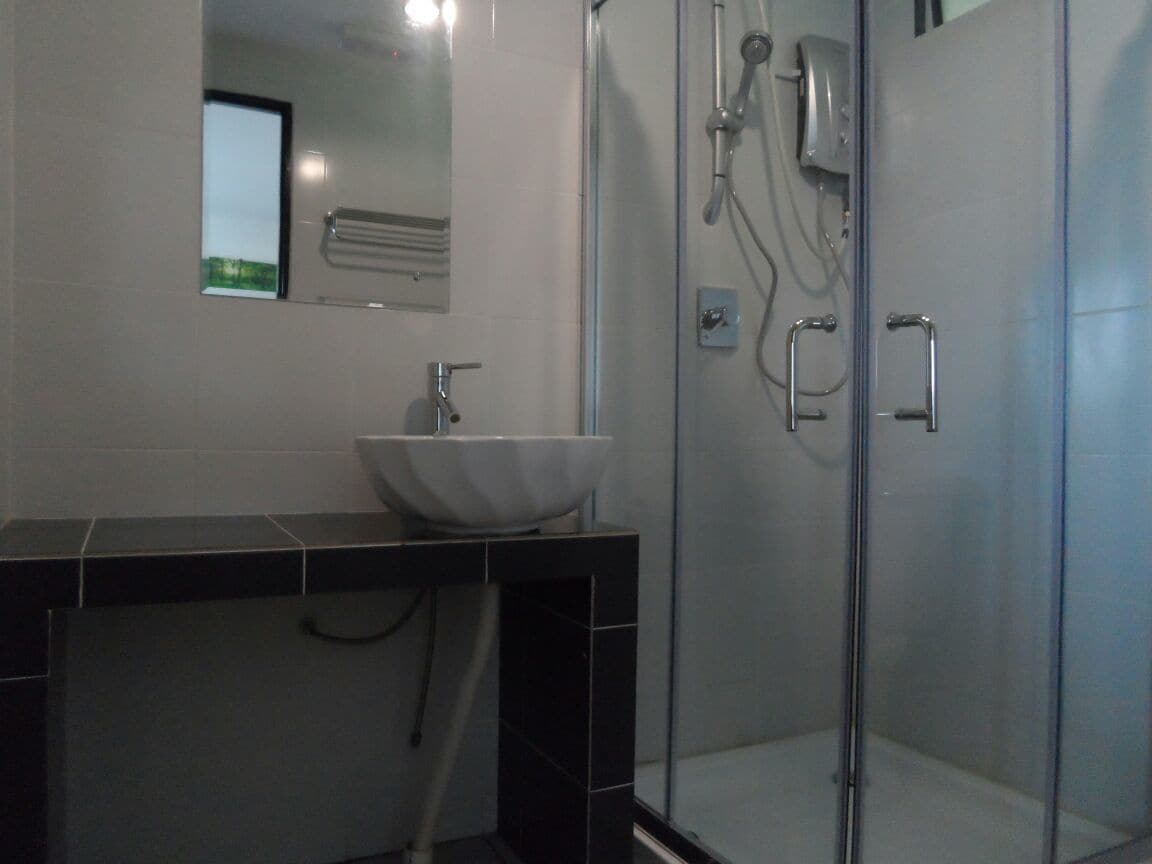 Un bagno moderno con cabina doccia in vetro, lavandino bianco e piano di appoggio nero.