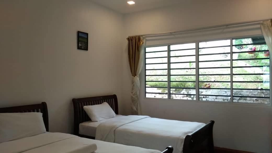 A room with two single beds, a window with bars, and a view of greenery outside.