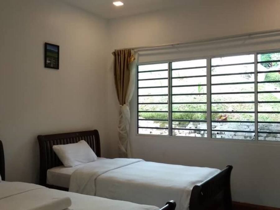 A room with two single beds, a window with bars, and a view of greenery outside.