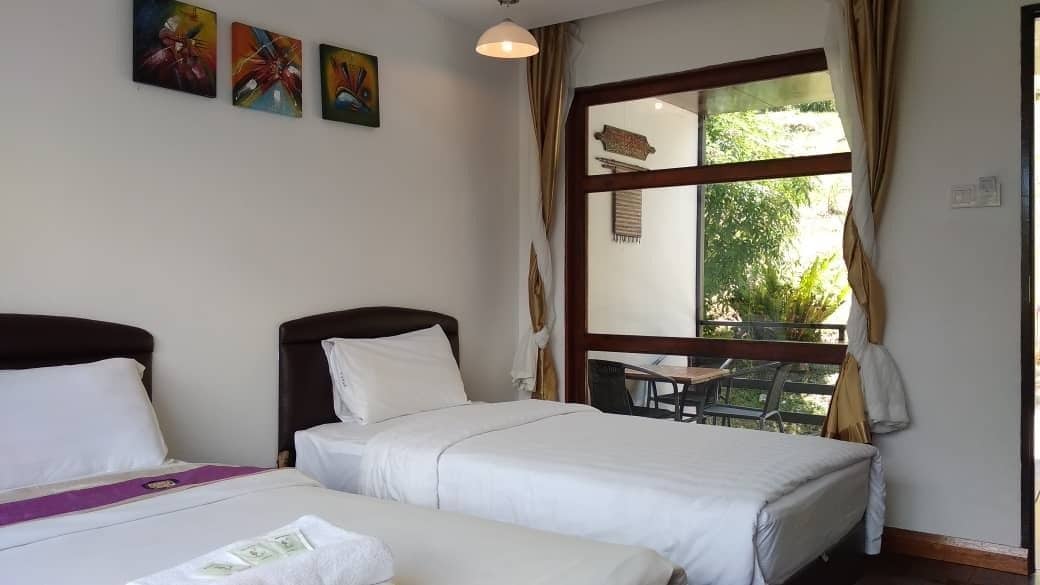 A hotel room with two beds, a dining table, and a large window with curtains.