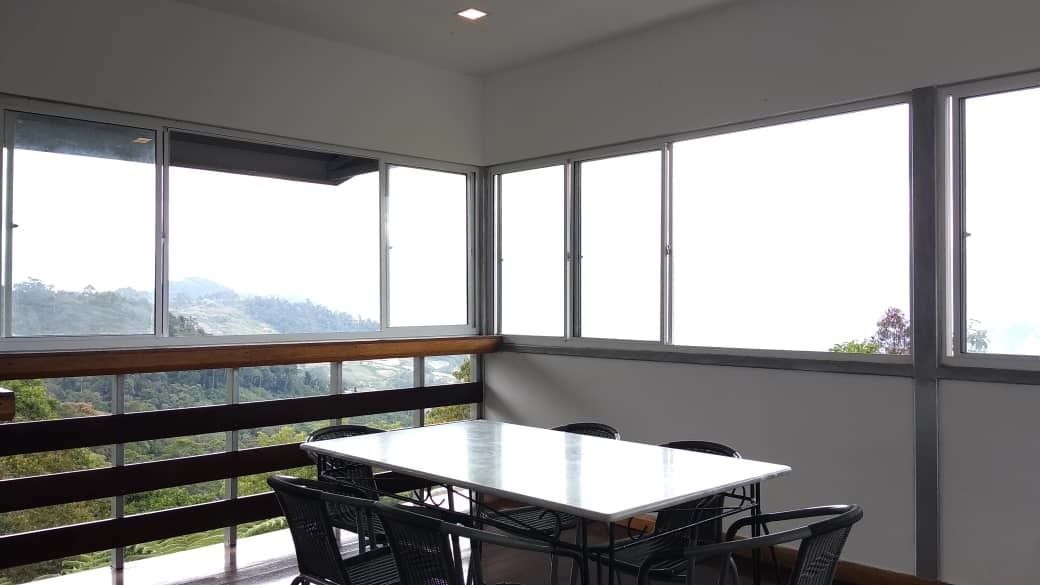 A room with a large window overlooking a mountainous landscape, a white table, and black chairs.