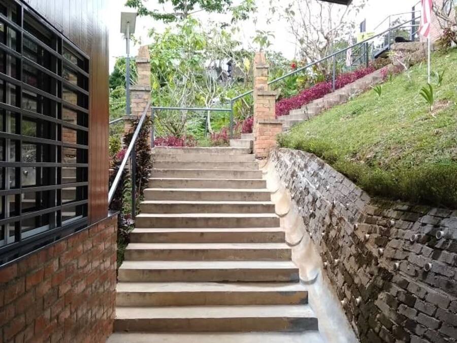 A staircase with a brick wall on one side and a metal railing on the other, leading to a building with a window grille.