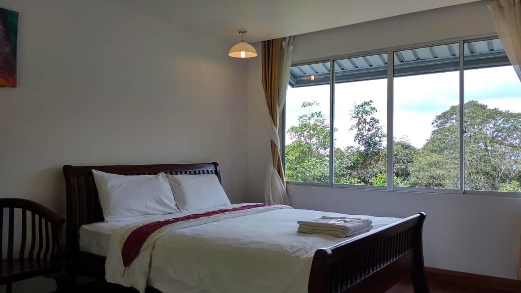 Quarto com cama, uma cadeira e janela com vista para árvores.