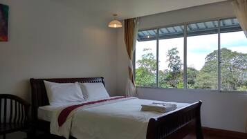 Quarto com cama, uma cadeira e janela com vista para árvores.