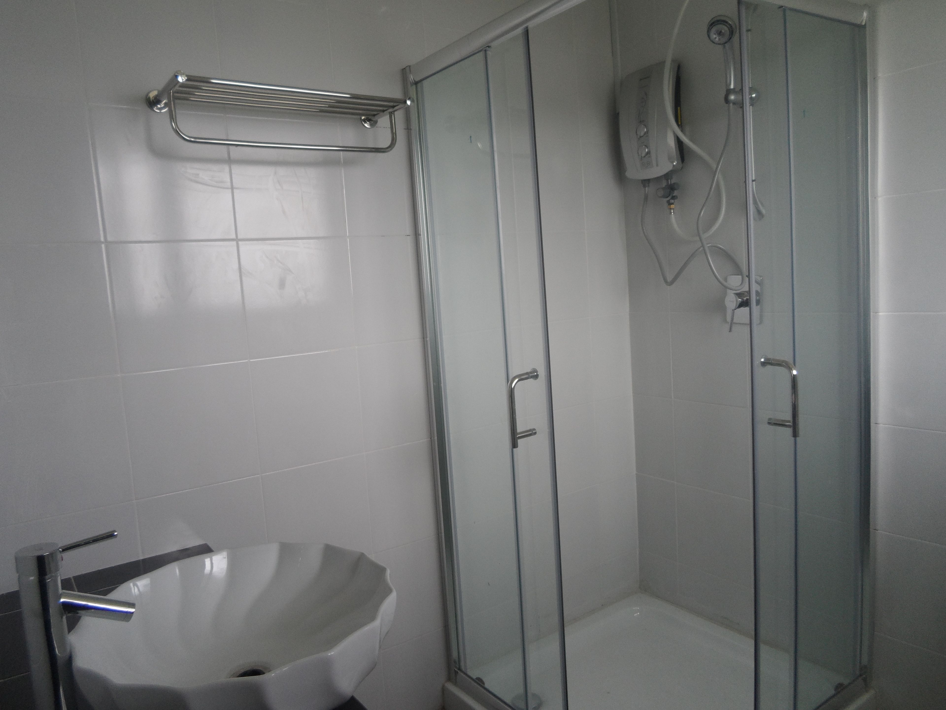 A modern bathroom with a glass shower enclosure, a white sink, and a towel rack.