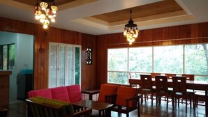 A dining area with wooden walls, a large window with a view of trees, and a chandelier.
