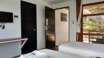 A hotel room with a bed, a desk, a TV, and a window with a view of a staircase and greenery.