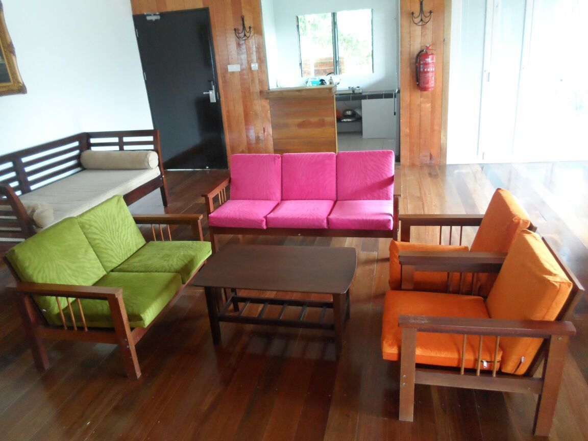 A room with a wooden floor, a wooden bench, a pink sofa, and an orange sofa.