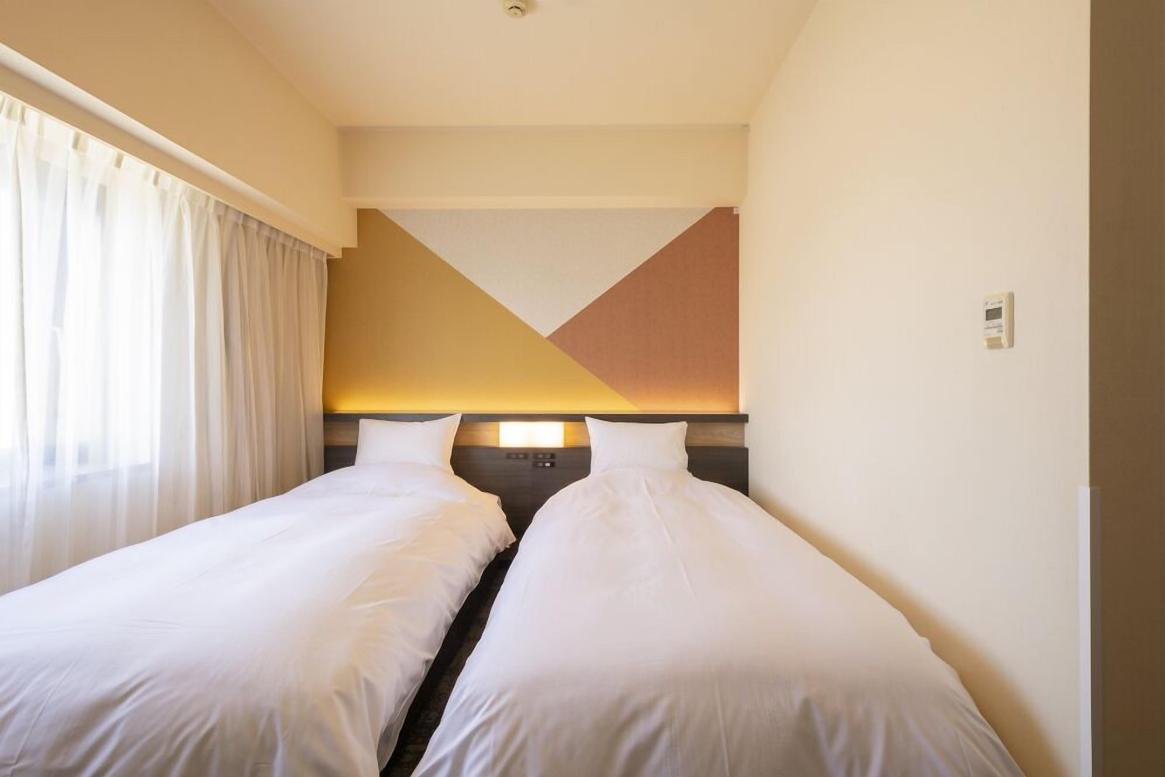 Une chambre d’hôtel avec deux lits simples, une décoration aux couleurs neutres et un design moderne.