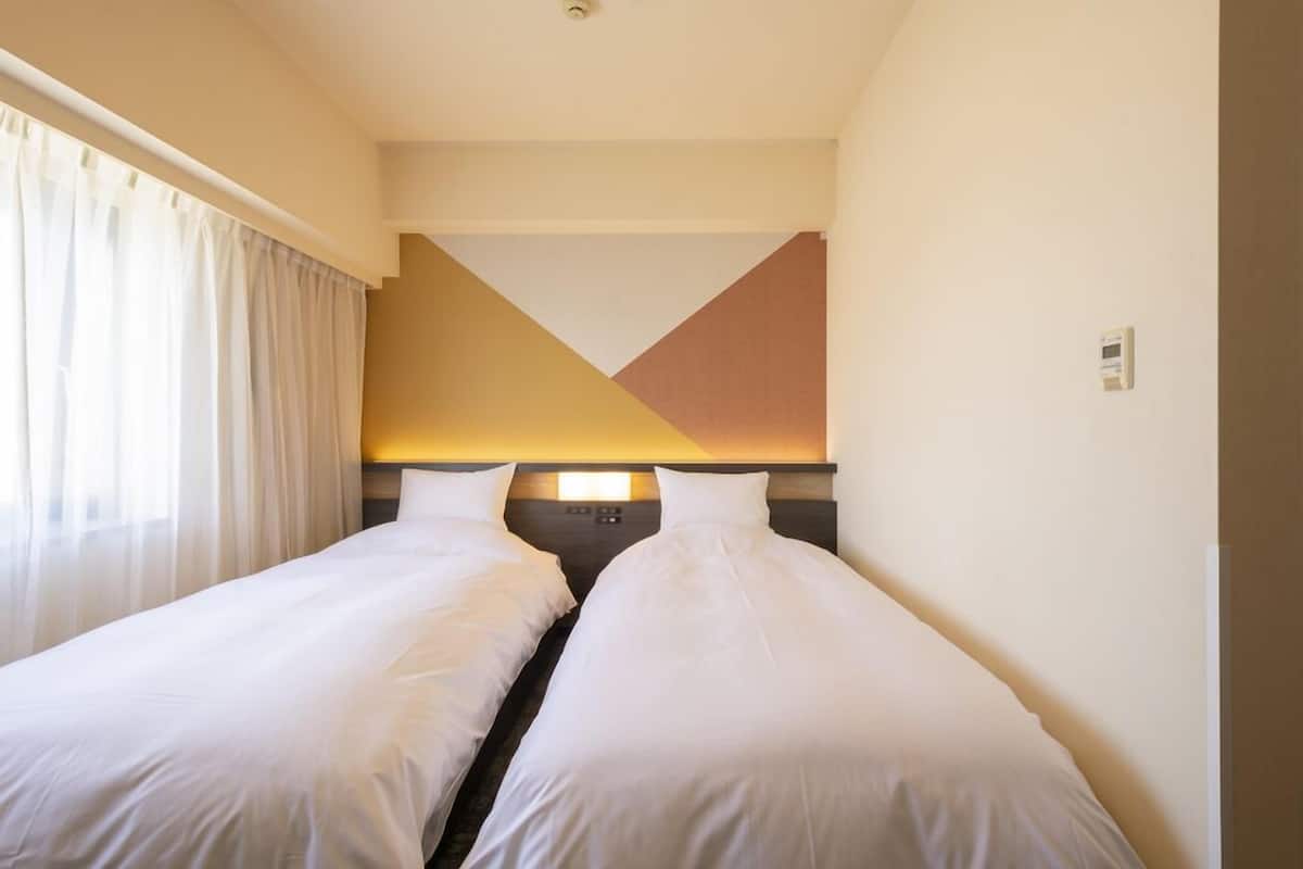 A hotel room with two single beds, a neutral color scheme, and a modern design.